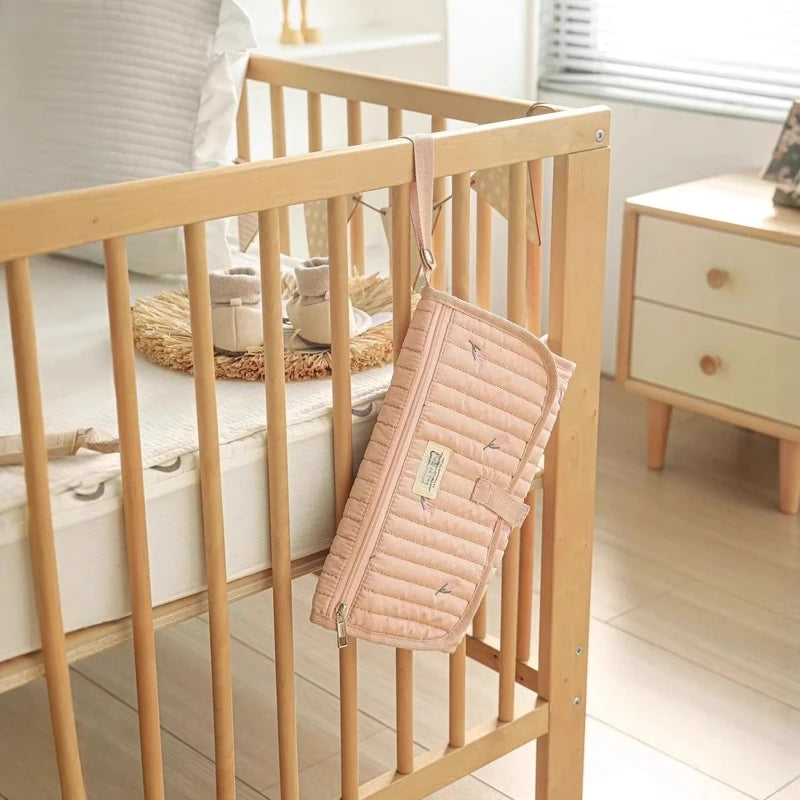 Tapis à langer de voyage  rose accroché sur le lit de bébé
