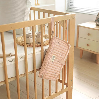 Tapis à langer de voyage  rose accroché sur le lit de bébé