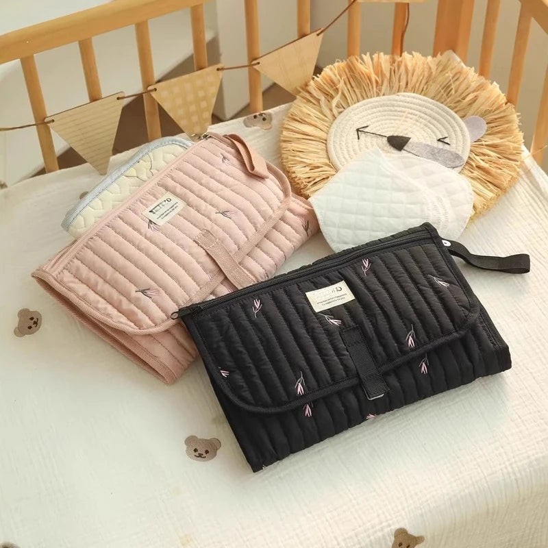 Tapis à langer de voyage  rose et noir exposés sur le lit de bébé