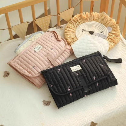 Tapis à langer de voyage  rose et noir exposés sur le lit de bébé