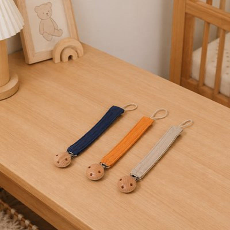 Attache tétine bleu marine, orange et beige posées sur la table 