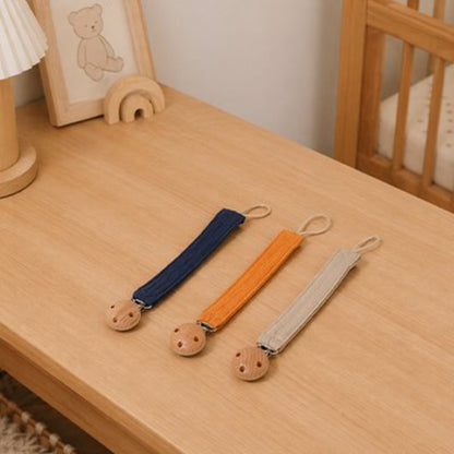 Attache tétine bleu marine, orange et beige posées sur la table 
