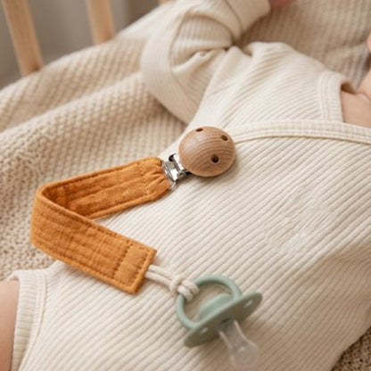 Attache tétine orange clipée sur le pyjama de bébé 