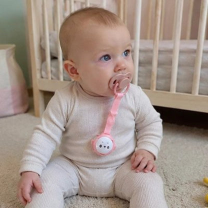 Attache tetine rose bébé assis sur le tapis dans sa chambre