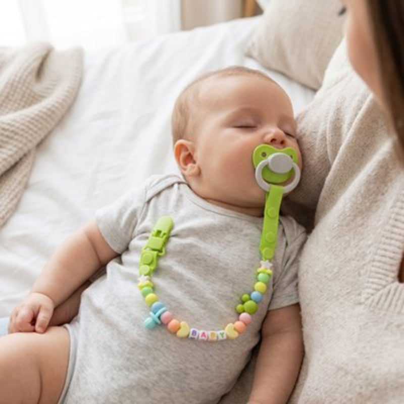 Attache tetine vert bébé qui dort dans les bras de sa maman