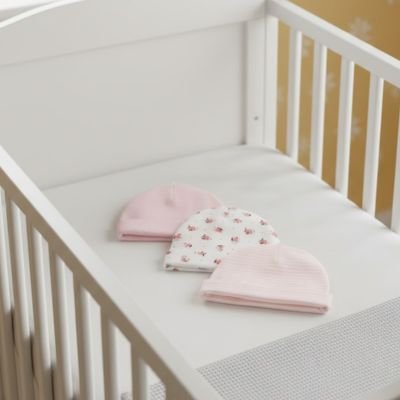 Bonnet bébé fille rose, blanc floral et trait rose et blanc posés sur le lit
