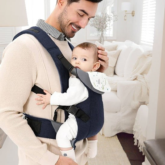Porte bébé bleu avec sangle noires, papa débout au salon portante confortablement son bébé 