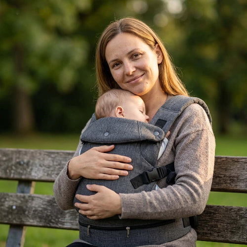 Porte bebe gris foncé bébé blotit contre sa maman assise au parc