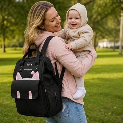 Sac a dos a langer noir, maman tenant son bébé souriant dans les mains