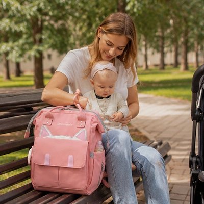 Sac a dos a langer rose, maman assise sur un banc avec son bébé