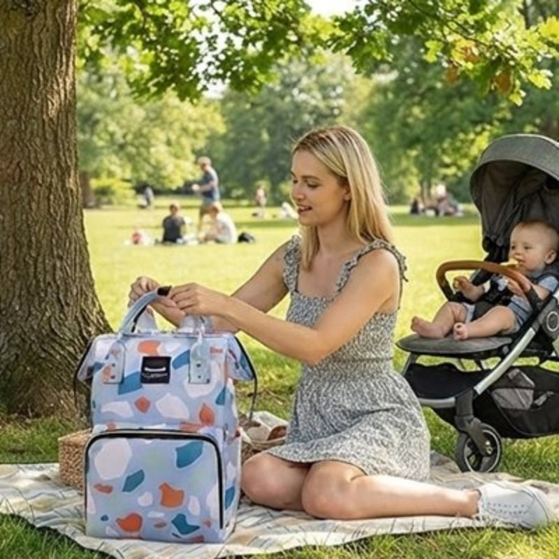 Sac a langer bebe bleu foncé maman assise sous l'arbre au parc avec son enfant dans la poussette