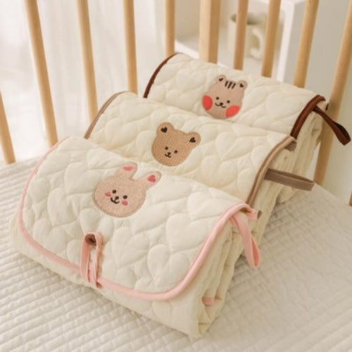 Tapis à langer nomade rose, beigeet brun posés sur le lit du bébé