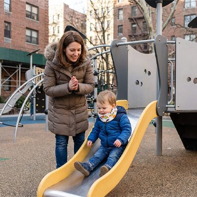 Tour de cou blanc/dinosaure bébé qui joue sur la glissade au parc avec sa maman